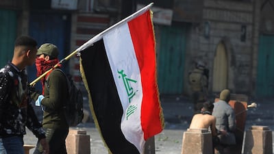 An Iraqi protester carries a national flag as others take cover behind a makeshift shield amid clashes with riot police following a demonstration at Al Wathba Square in the capital Baghdad, on January 30, 2020. AFP