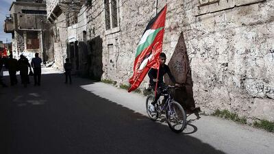 A Palestinian boy rides a bicycle holding his national flag as others demonstrate in the centre of the West Bank city of Hebron against the closure of the main downtown street Al-Shuhada and also to mark the 20th anniversary of the massacre of 29 Palestinian Muslim worshipers by Jewish at the Tomb of the Patriarchs. Thomas Coex / AFP