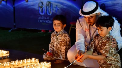 A man and two children light candles after the building lights were switched off for the Earth Hour environmental campaign in Dubai on March 24, 2018. Earth Hour, which started in Australia in 2007, is set to be observed by millions of supporters in 187 countries, who will turn off their lights at 8.30pm local time in what organisers describe as the world's "largest grassroots movement for climate change". / AFP PHOTO / Giuseppe CACACE