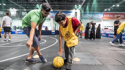 A coach helps a boy dribble the ball during basketball training.