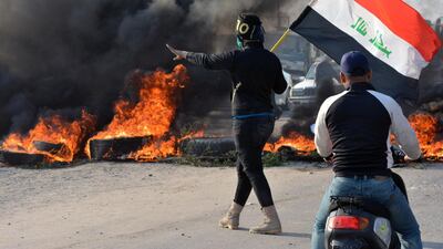 A demonstrator holds an Iraqi flag near burning tires during ongoing anti-government protests in Nassiriya, Iraq. Reuters
