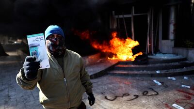 A protestor stands in front of burning tyres and Arabic graffiti on the ground that reads 'thieves' outside a bank in Beirut. AFP