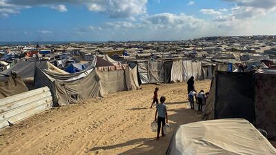 Palestinian children carry water jugs past tents housing displaced people in the Mawasi area of Khan Younis in the southern Gaza Strip on August 7, 2025. The UAE has criticised Israeli plans to occupy Gaza 'in the strongest terms'. AFP