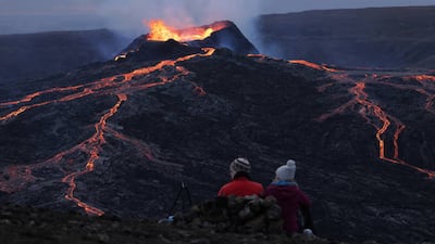A couple sitting on a hill watch as the Fargradalsfjall volcano spews molten lava. Getty Images
