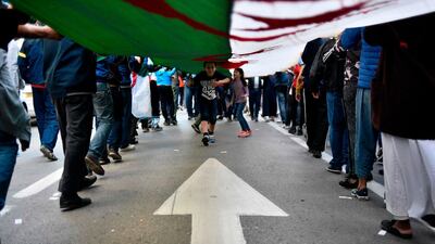 Algerian children run beneath a giant unfurled national flag carried by protesters marching during the 36th consecutive Friday anti-government demonstrations in the capital Algiers. AFP