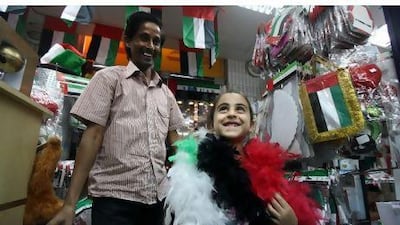 Mohammed al Din helps Jana al Jammal, 6, with a UAE coloured scarf at his shop in Abu Dhabi. Sammy Dallal / The National