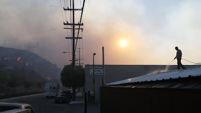 A man uses a garden hose to water down a rooftop as the Tick Fire burns nearby in Canyon Country. AFP