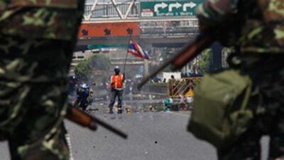 An anti-government demonstrator holds a Thai flag in front of soldiers at a main street in central Bangkok today.