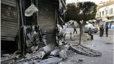 Syrian soldiers, right, patrol near a shop burned in Sunday's clashes between protesters and security forces in Latakia.