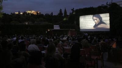 People watch the movie The Immigrant at the Thisio outdoor summer cinema as the Ancient Acropolis is seen lit up in the background.