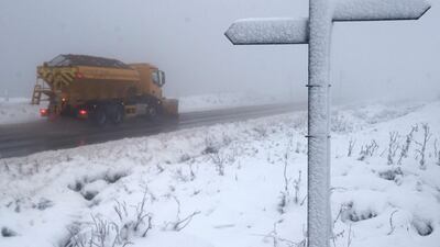 A signpost marking the Pennine Way footpath is in covered with snow as a gritting lorry drives along the A62 above the village of Delph. AFP