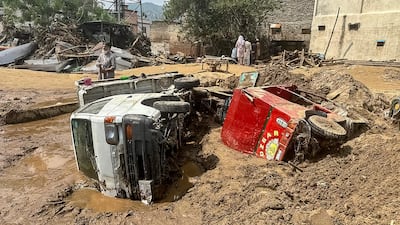 People walk past damaged vehicles and scattered debris. AFP