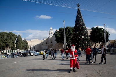 A Palestinian man wearing a Santa Claus costumes welcomes Christian visitors outside the Church of the Nativity, traditionally believed by Christians to be the birthplace of Jesus Christ, in the West Bank city of Bethlehem. AP