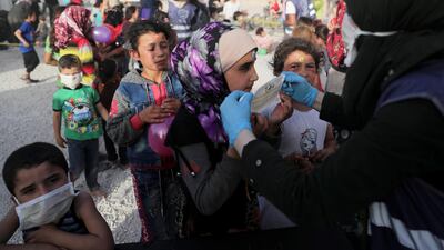 A volunteer from the International Association for Relief and Development (ONSUR) distributes face masks to internally displaced children, ahead of the Eid al-Fitr holiday, at an IDP camp in Idlib, Syria. Reuters