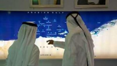 Two men chat in front of an Arabian Gulf map inside the Adnoc showroom at the Abu Dhabi International Petroleum Exhibition & Conference.
