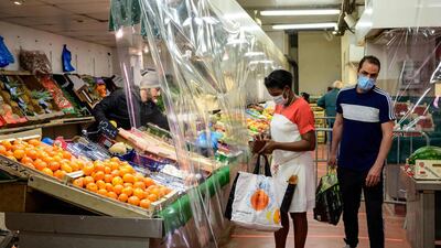 People wearing protective facemasks fot their grocery shopping next to fruits and vegetables stalls at a covered market in Le Perreux-sur-Marne. AFP