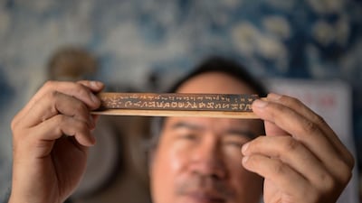 This photo taken on June 11, 2019 shows cultural advocate Leo Emmanuel Castro holding a piece of bamboo inscribed with indigenous Baybayin script at his shop in Manila. From tattoos, shirts, and artworks to a computer font and mobile apps, Baybayin found a rebirth among millennials and professionals learning its 17 characters beyond the marginal mention in history class.