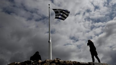 Tourists stand beneath a huge Greek flag in front of a broken ancient marble column at the Acropolis hill, in Athens. Petros Giannakouris / AP