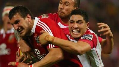 Lions captain Sam Warburton, left, is tackled by Reds skipper Quade Cooper, centre, during Saturday’s match in Brisbane. Patrick Hamilton / AFP