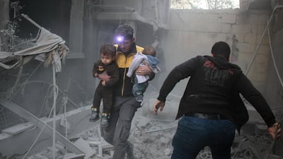 A Syrian man carries two children from the rubble of buildings destroyed by Syrian government air strikes in Douma on February 7, 2018. Hamza Al Ajweh / AFP