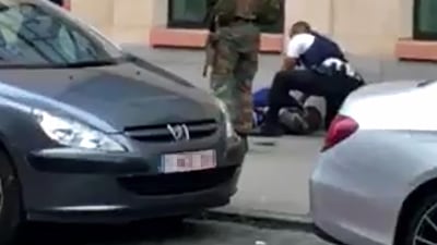 This screengrab shows police officials and a soldier looking at a man on the pavement in the city centre of Brussels, where a man is alleged to have attacked soldiers with a knife and was shot. AFP PHOTO / Belga / STR / Belgium OUT