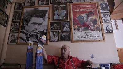 A man stacks popcorn boxes beside movie posters of the 1955 drama Rebel Without a Cause and the 1939 historical romance Gone with the Wind at the canteen of the Thisio outdoor summer cinema, near the ancient Acropolis in Athens. Cine Thisio is one of the oldest open-air movie theatre in Athens, built in 1935.