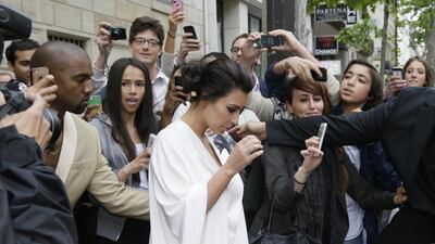 People gather around Kim Kardashian, centre, and Kanye West, left, as they leave their residence in Paris on May 23, 2014, before their wedding. AFP