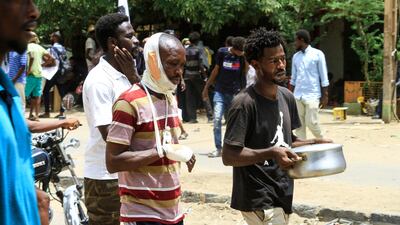 A wounded Sudanese demonstrator follows a protester carrying a pot of food. AFP