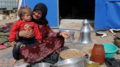 An internally displaced woman with a child on her lap prepares food outside a tent in Azaz, Syria. REUTERS