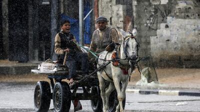 A Palestinian man and child ride a donkey-drawn cart amidst heavy rain in Rafah in the southern Gaza Strip on February 9, 2020. / AFP / Said KHATIB