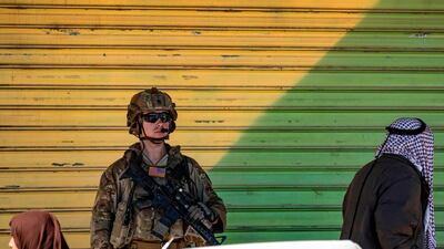 People walk past a US soldier standing in the town of Tal Tamr along the M4 highway in the northeastern Syrian Hasakeh province, near the border with Turkey. AFP