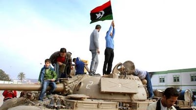 Residents stand on a tank holding a pre-Qaddafi era Libyan flag inside a security forces compound in Benghazi.