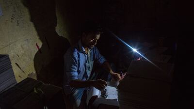 A man uses his mobile phone torch to work at a printing press during a load-shedding power outage.