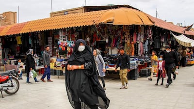 Iranians, some wearing personal protective equipment, walk past shops in the southeastern city of Kerman, Iran. AFP