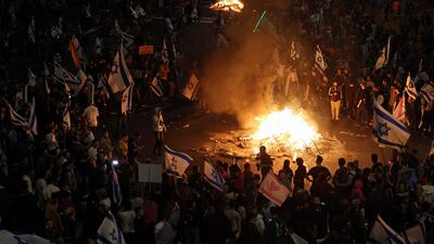 The protesters in Tel Aviv hold Israeli flags as they gather around a bonfire. AFP