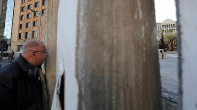 An anti-government protester peers through a gap in a concrete wall installed by authorities to keep protesters far from the main Lebanese government headquarters, far right, and open road to parliament, in downtown Beirut, Lebanon. AP Photo