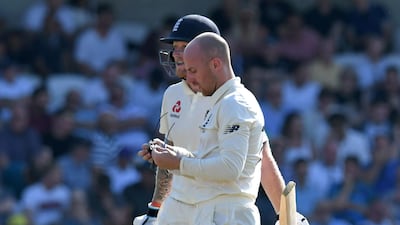 Jack Leach cleans his glasses as he and England's Ben Stokes speak during a break in play. AFP
