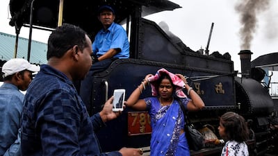 Passengers stand next to a Darjeeling Himalayan Railway steam train as it halts briefly at Batasia Loop.