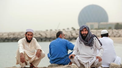 Pakistani delivery truck drivers take a break by the sea on a dusty day in Abu Dhabi. Victor Besa / The National