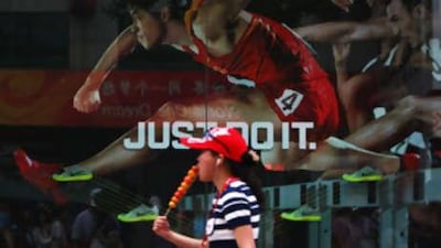 A Chinese woman eats snack as she walks past an advertisement featuring defending Olympic 110 metres hurdles champion Liu Xiang.