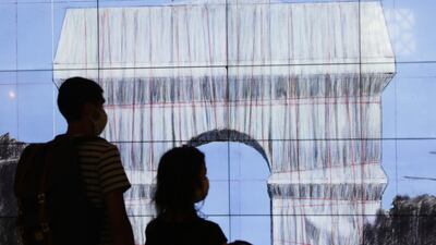 Visitors watch a video on "L'Arc de Triomphe, Wrapped" in Paris, Tuesday, Aug. 24, 2021. The "L'Arc de Triomphe, Wrapped" project by late artist Christo and Jeanne-Claude will be on view from, Sept. 18 to Oct. 3, 2021. The famed Paris monument will be wrapped in 25,000 square meters of fabric in silvery blue, and with 3,000 meters of red rope. (AP Photo / Adrienne Surprenant)