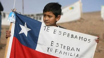 A young boy holds a Chilean flag reading "We wait for you Esteban, Your Family".