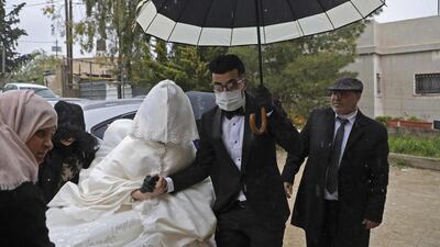 Palestinian groom Imad Sharaf, wearing gloves and a face mask, accompanies his bride Bara'a Amarneh as they arrive at their home in the village of al-Dahriya, south of Hebron in the West Bank, on March 20, 2020. AFP
