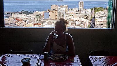 A woman eats lunch near a window overlooking Copacabana beach at the Bela Vista Bar located in the Pavao-Pavaozinho slum in Rio de Janeiro