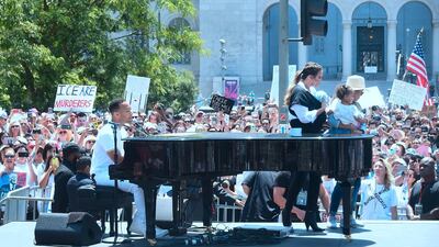 John Legend sings at the piano as Chrissy Teigen, holding their baby, walks off stage during a 'Familes Belong Together' march and rally in Los Angeles, California. AFP
