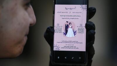 Issam Sharaf, brother of Palestinian groom Imad, holds up a phone showing an electronic image of a wedding invitation with a cartoon of both the bride and groom wearing protective masks, at their home in the village of al-Dahriya, south of Hebron in the West Bank. AFP