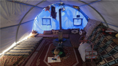 Mahmoud Abdel Hadi, an 8-year old refugee, studies inside his tent after the pandemic forces schools to close. He uses a mobile phone to check instructions for his homework. Photo by Khalil Ashawi