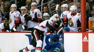 Ottawa Senators' Alex Burrows checks Vancouver Canucks' Troy Stecher through the open door and into the Ottawa bench during the first period of an NHL hockey game in Vancouver, British Columbia. Darryl Dyck / The Canadian Press via AP