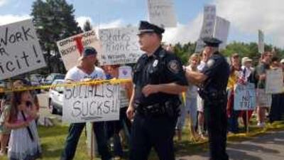 Police stand near protesters outside Portsmouth High School in New Hampshire, where Barack Obama is holding a town hall meeting.