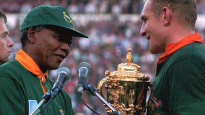 South African rugby captain Francios Pienaar, right, receives the Rugby World Cup trophy from President Nelson Mandela, left, who wears a South African rugby shirt, after South Africa defeated New Zealand in Johannesburg, in this June 1995 photo.